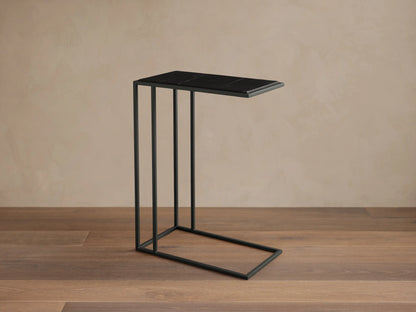 Mills Stone C Table: Matte black C-style steel frame supports a rectangular dark stone top with subtle natural veining on a wood floor.
