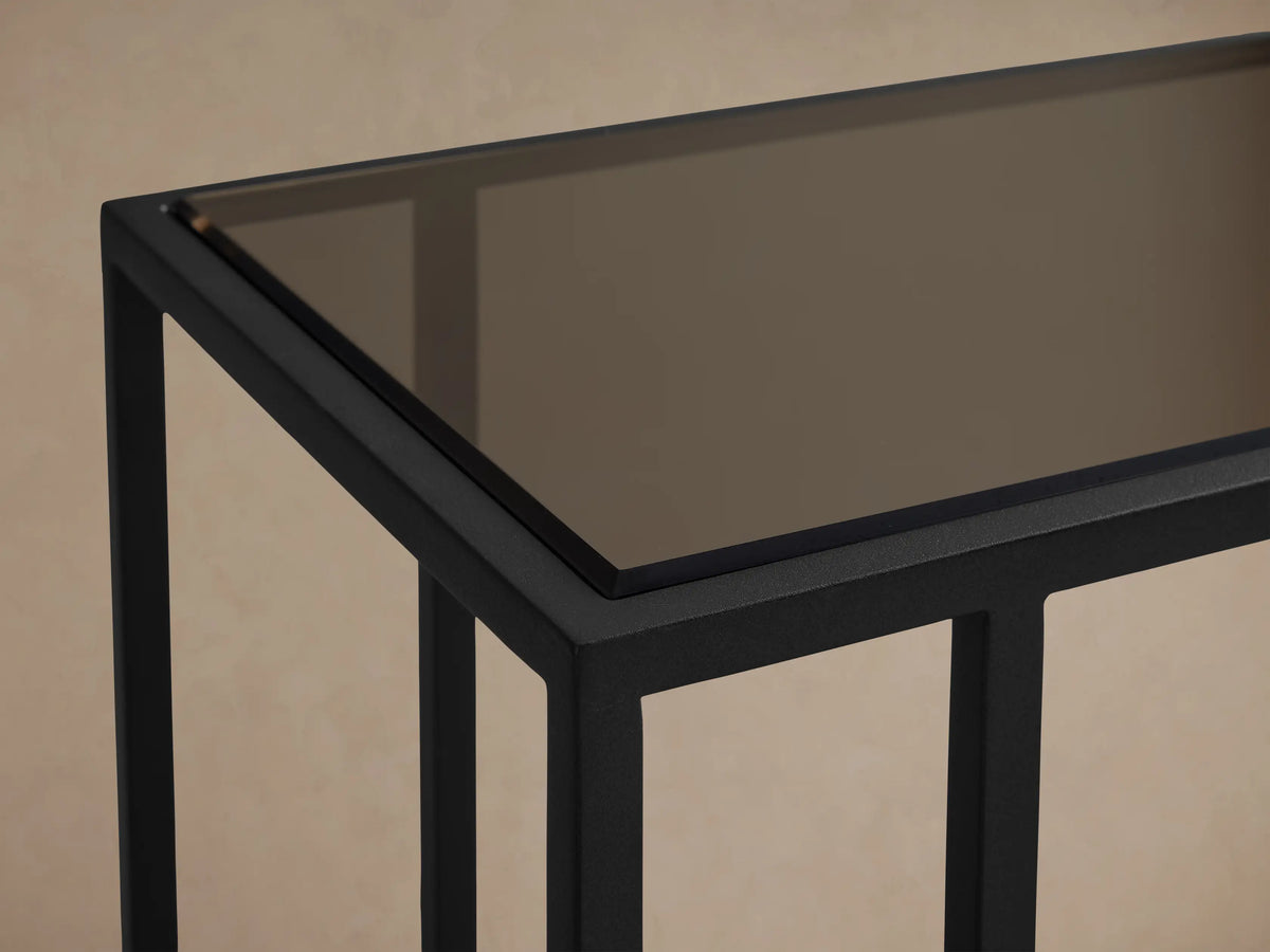 Close-up, angled view of the Mills Glass C Table, featuring its rectangular smoked glass top and matte black steel frame.