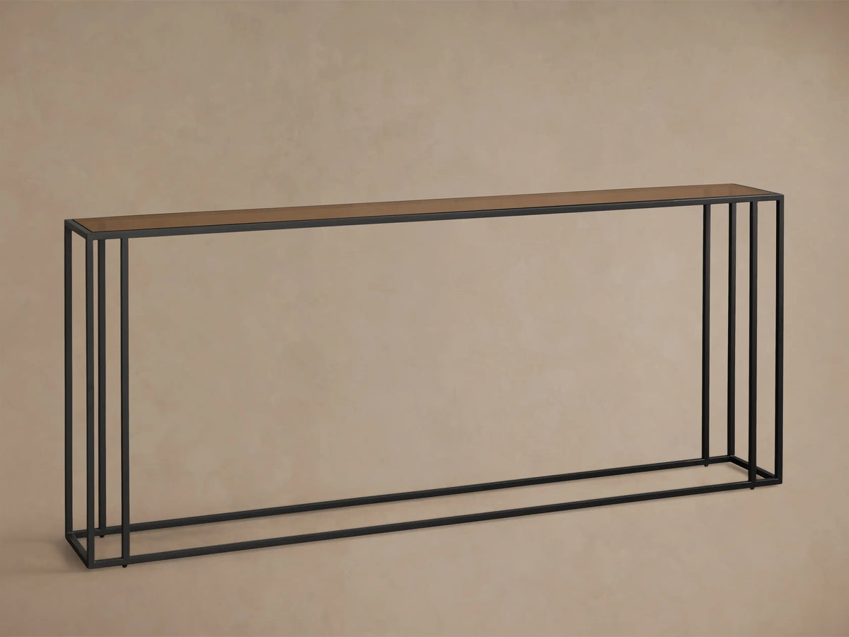 Front view of the long, narrow Mills Glass Console Table with an antique brass-toned glass top and matte black steel frame.
