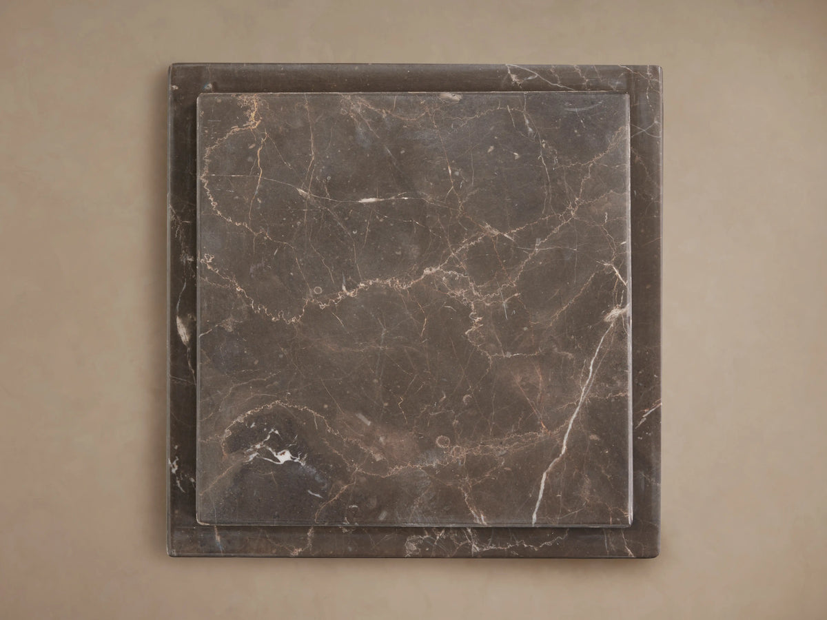 Three grey marble Marmont Pedestals of varying heights on a wood floor against a light wall, featuring natural white veining.