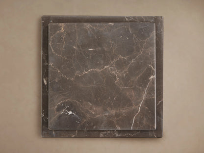 Three grey marble Marmont Pedestals of varying heights on a wood floor against a light wall, featuring natural white veining.