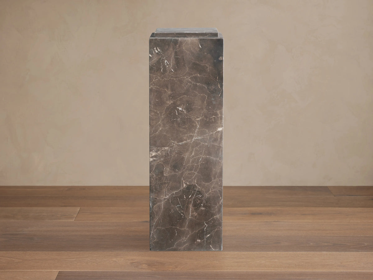 Marmont Pedestal made of natural marble with a matte finish, showing unique veining. Tall, rectangular shape on wooden floor.