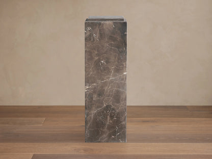 Marmont Pedestal made of natural marble with a matte finish, showing unique veining. Tall, rectangular shape on wooden floor.