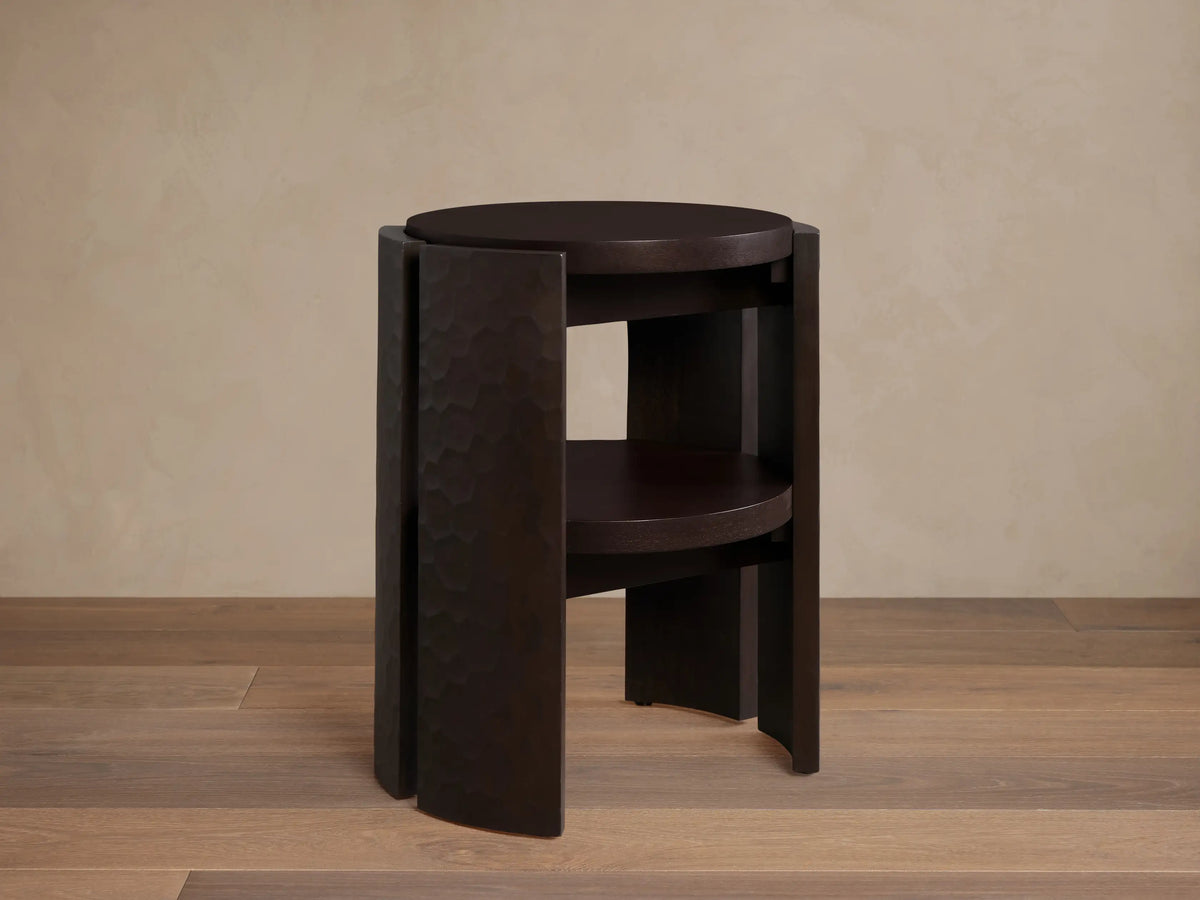 Dark mahogany Chiseled End Table with two round shelves. Features textured, hand-carved wood legs, standing on a wood floor.
