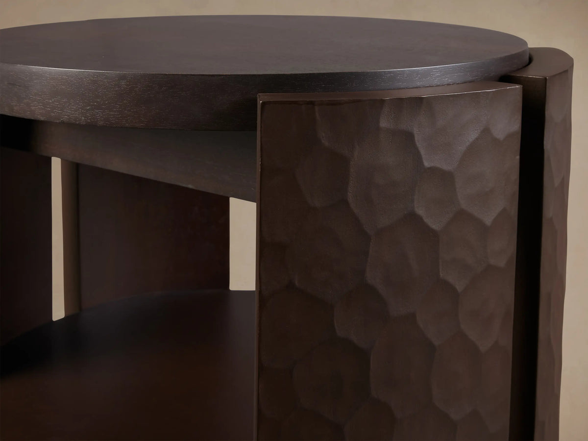 Dark brown Chiseled End Table, close-up. Round top, lower shelf, side panel with deep, irregular chiseled texture.
