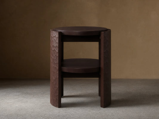 Dark brown Chiseled End Table with a round top and shelf, featuring deeply textured hand-carved legs, on a wood floor.