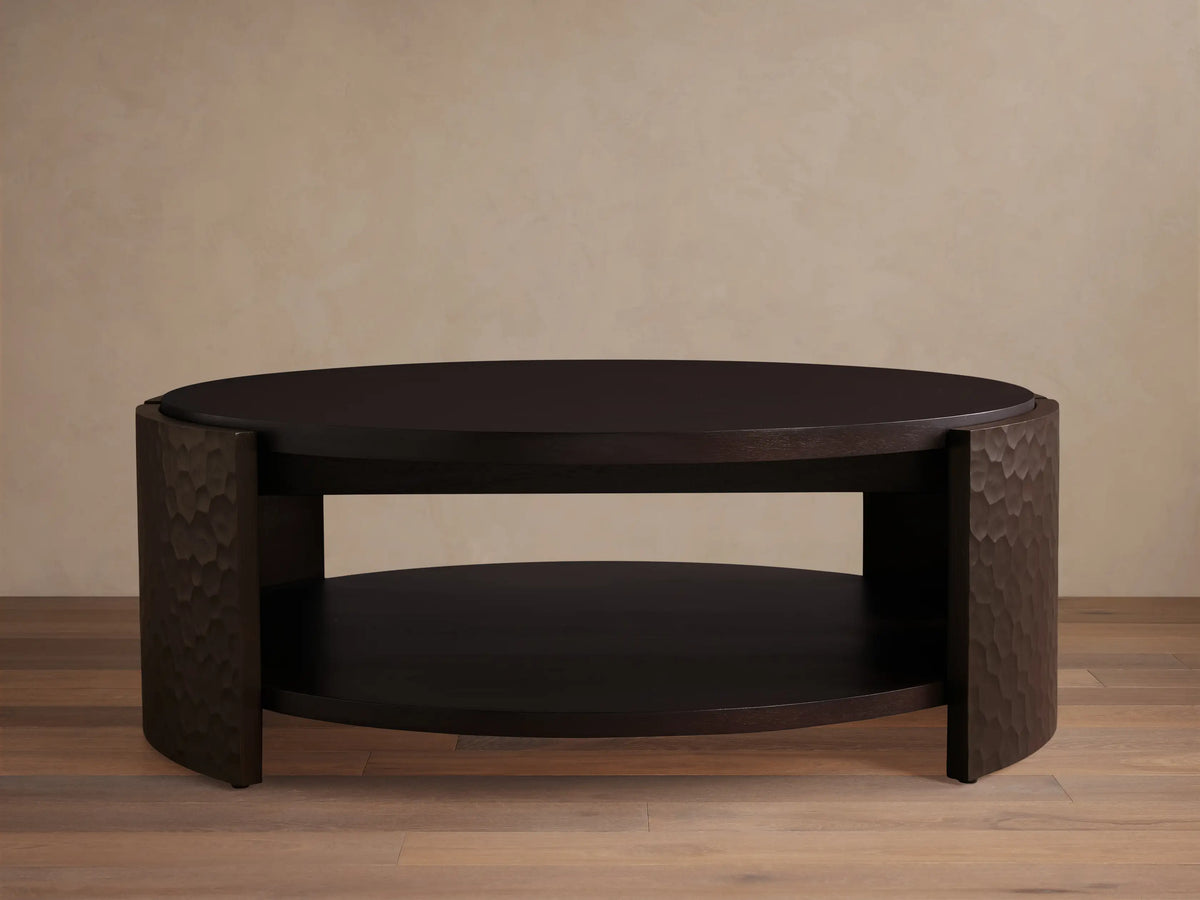 Dark mahogany chiseled round coffee table with two circular shelves and curved, textured side supports.