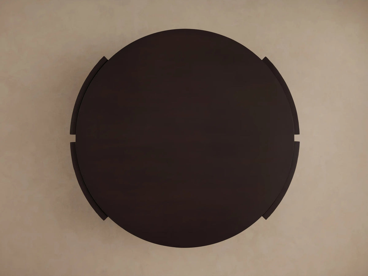 Dark brown mahogany Chiseled Round Coffee Table, showing the round top, lower shelf, and hand-carved textured sides.