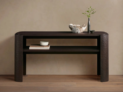 Dark brown mahogany Chiseled Console Table with rounded top, lower shelf. Legs feature distinct chiseled texture. Styled with decor.