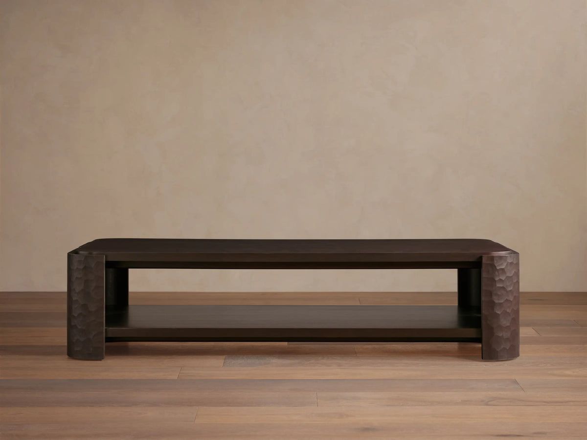 Dark mahogany Chiseled Coffee Table, two-tiered, with artisan hand-carved legs, on a wooden floor.