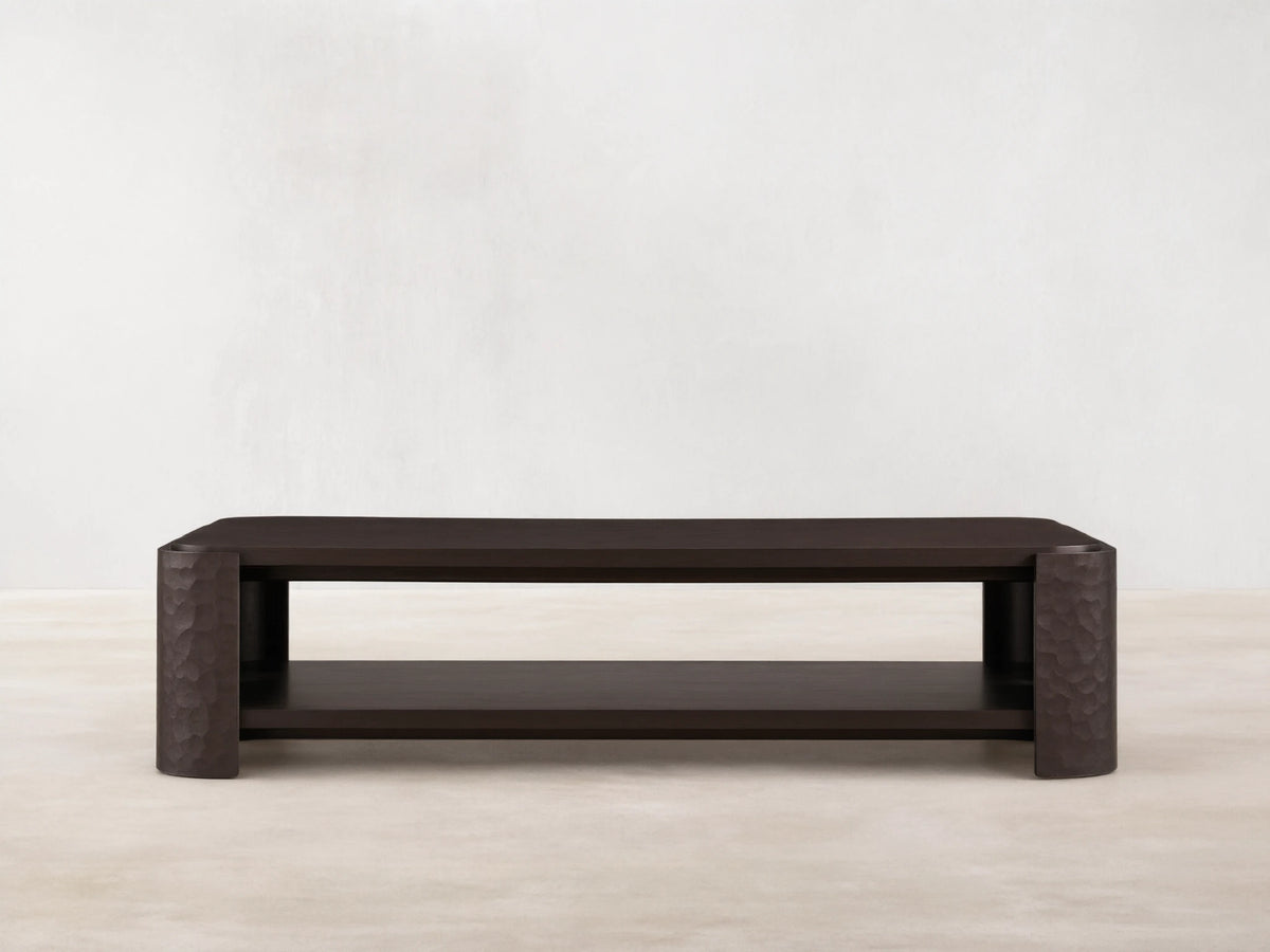 Dark mahogany Chiseled Coffee Table, two-tiered, with artisan hand-carved legs, on a wooden floor.