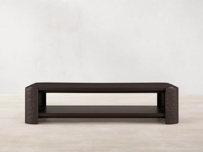 Dark mahogany Chiseled Coffee Table, two-tiered, with artisan hand-carved legs, on a wooden floor.