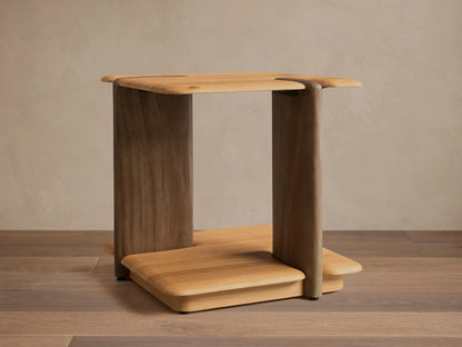 Front view of a light brown wooden side table, featuring a flat top and base with rounded edges, supported by a wide slab and a rounded leg.