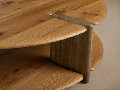 Nolito Coffee Table: Round, two-tiered, light natural wood shelves with visible grain & dark curved supports, on wooden floor.