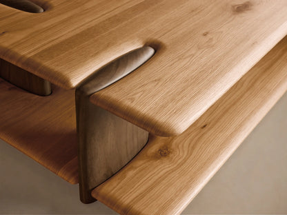 Front view of a light brown wooden coffee table with a rectangular top, lower shelf, integrated curved supports, and sculpted groove details.