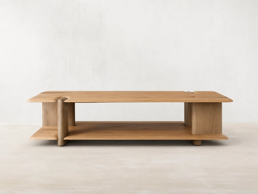 Front view of a light brown wooden coffee table with a rectangular top, lower shelf, integrated curved supports, and sculpted groove details.