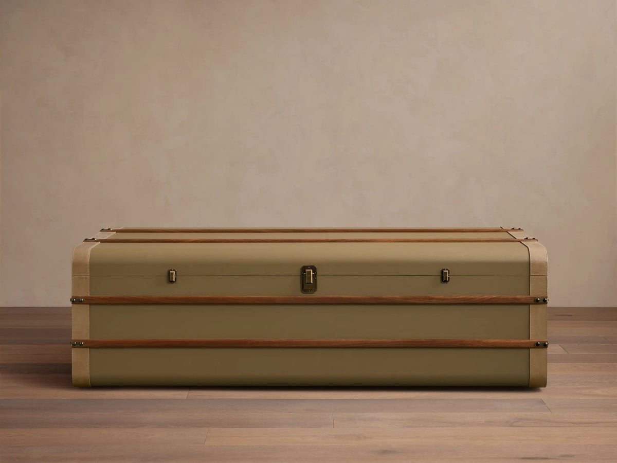 Front view of the olive Oberlin Storage Coffee Table, a trunk-style table with beige leather trim, a brass-tone lock, and wooden bands.