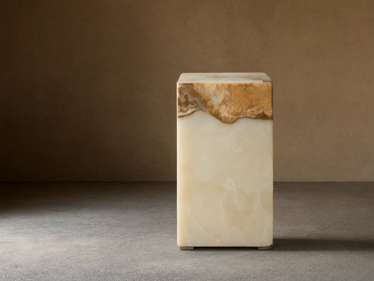 Rust Onyx Stool: rectangular block with a prominent horizontal band of rustic brown/gold/red onyx atop smooth ivory/green onyx, on a wood floor.