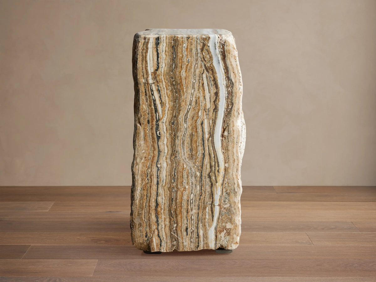 Solid Onyx Stool with vertical raw edges, showcasing natural brown and beige striations, sits on a wooden floor.