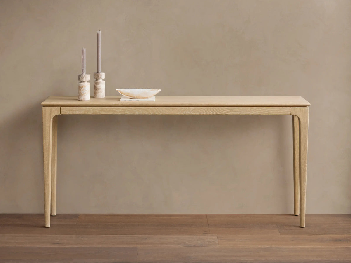 Long, narrow Park Console Table in light oak, with slender, curved legs. Two candles and a decorative bowl sit on top.
