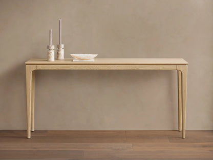 Long, narrow Park Console Table in light oak, with slender, curved legs. Two candles and a decorative bowl sit on top.