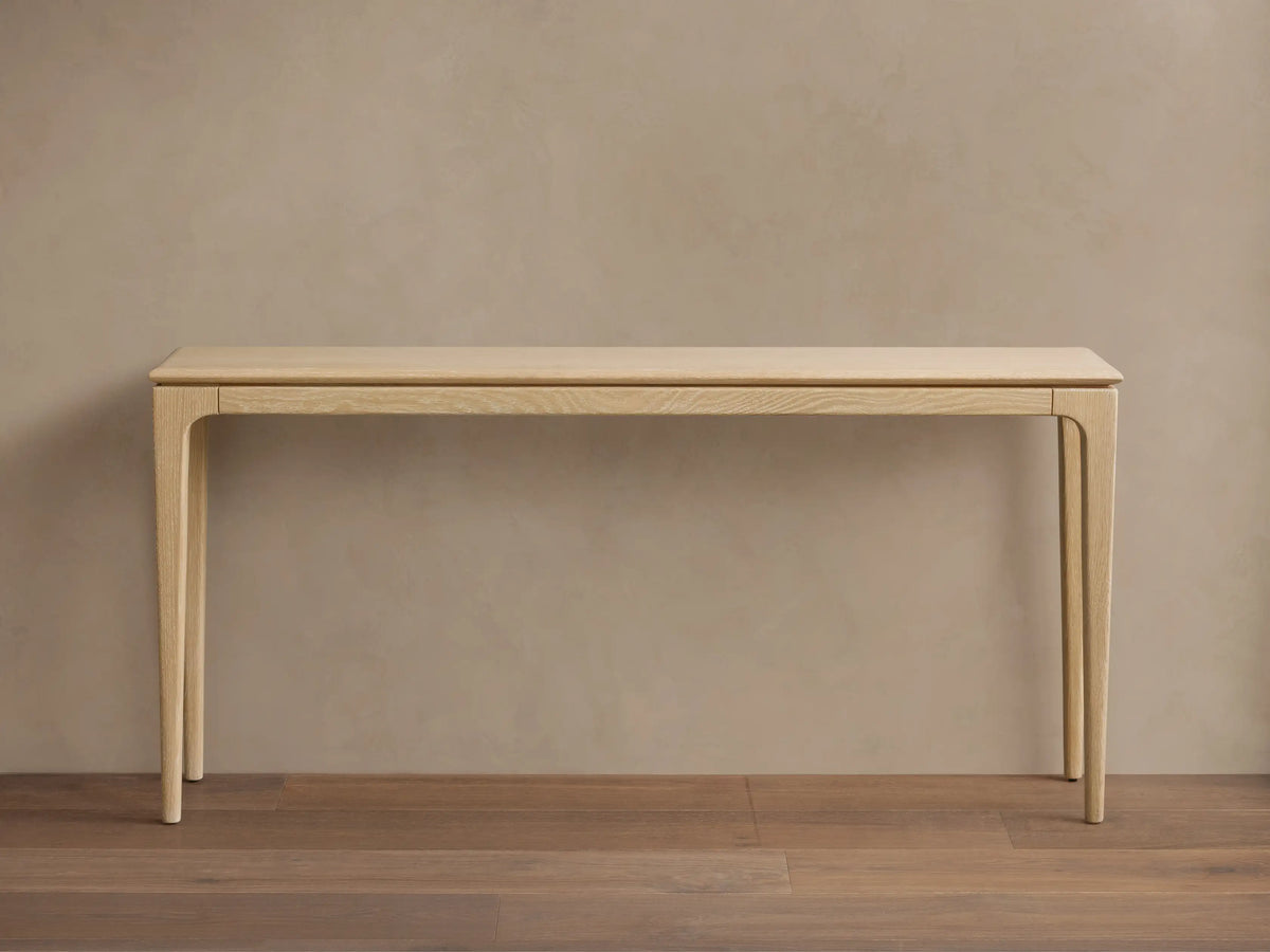 Long, narrow Park Console Table in light oak, with slender, curved legs. Two candles and a decorative bowl sit on top.