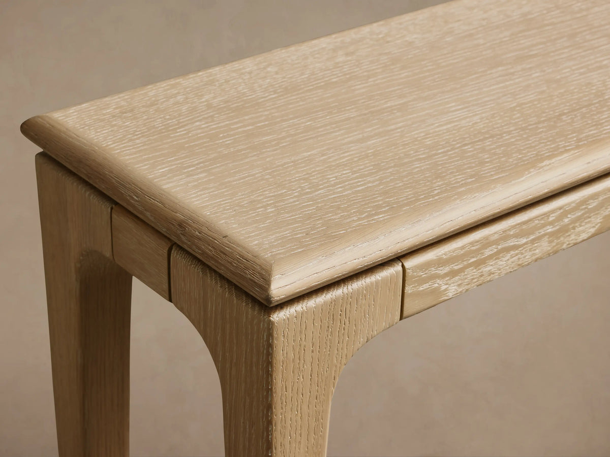 Light oak Park Console Table with thin top and slender legs, front view against a light brown wall and wooden floor.