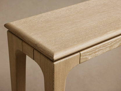 Light oak Park Console Table with thin top and slender legs, front view against a light brown wall and wooden floor.