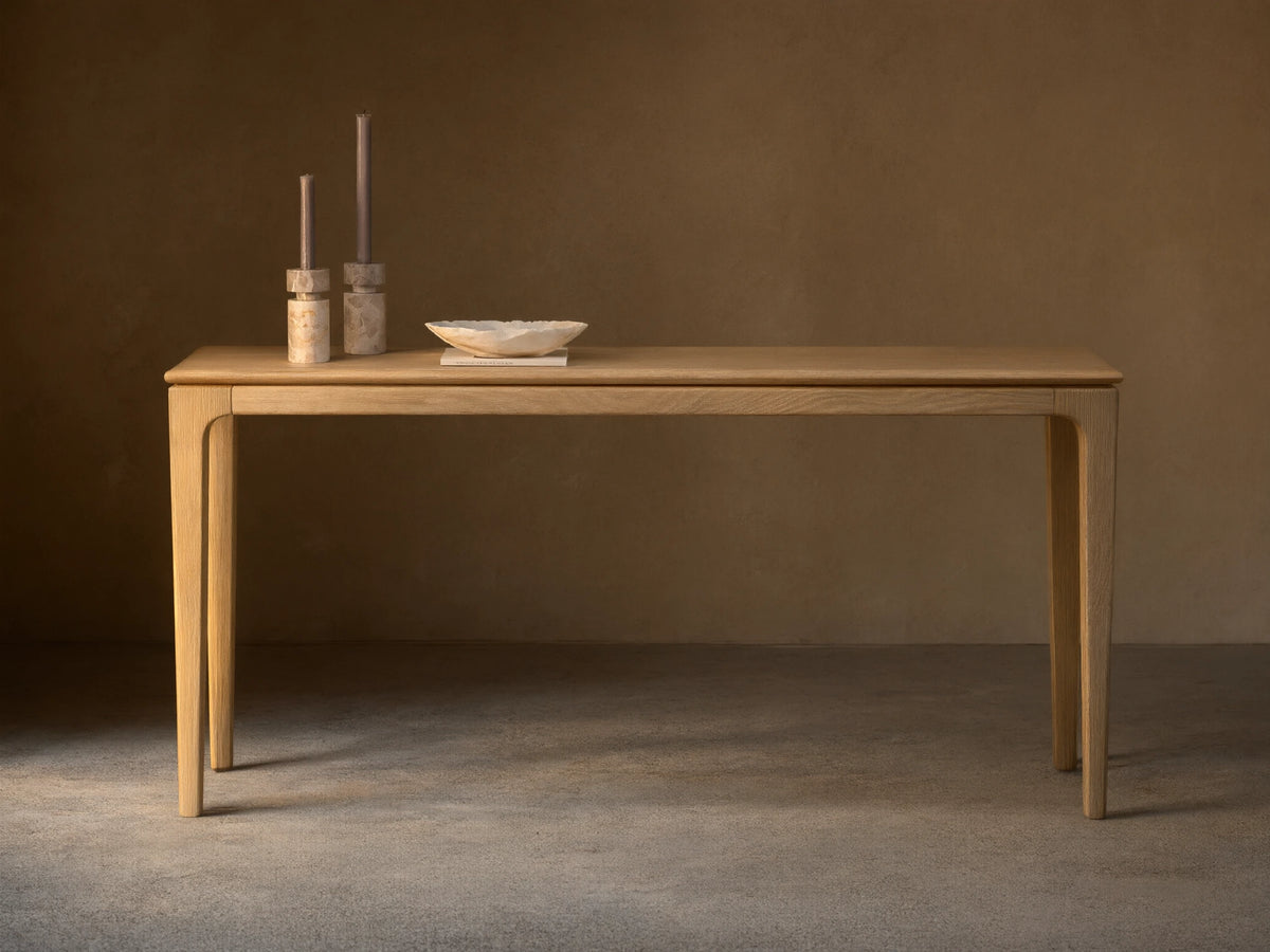 Long, narrow Park Console Table in light oak, with slender, curved legs. Two candles and a decorative bowl sit on top.