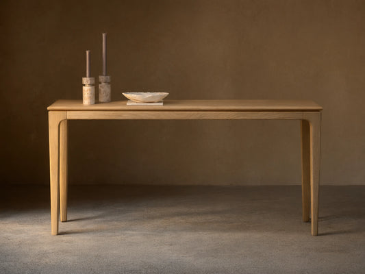 Long, narrow Park Console Table in light oak, with slender, curved legs. Two candles and a decorative bowl sit on top.