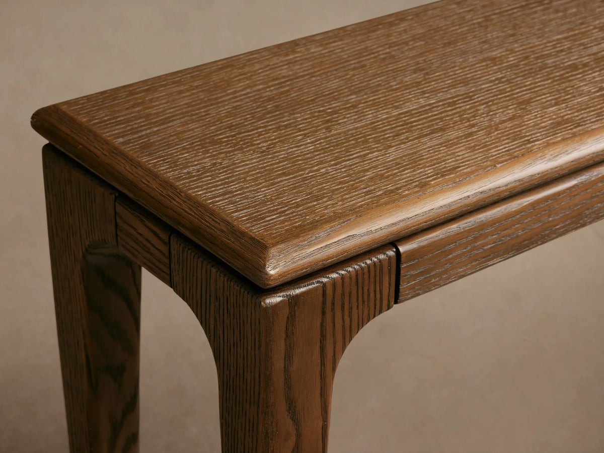 Long, narrow, dark brown Park Console Table with tapered wooden legs, against a light wall and wood floor.