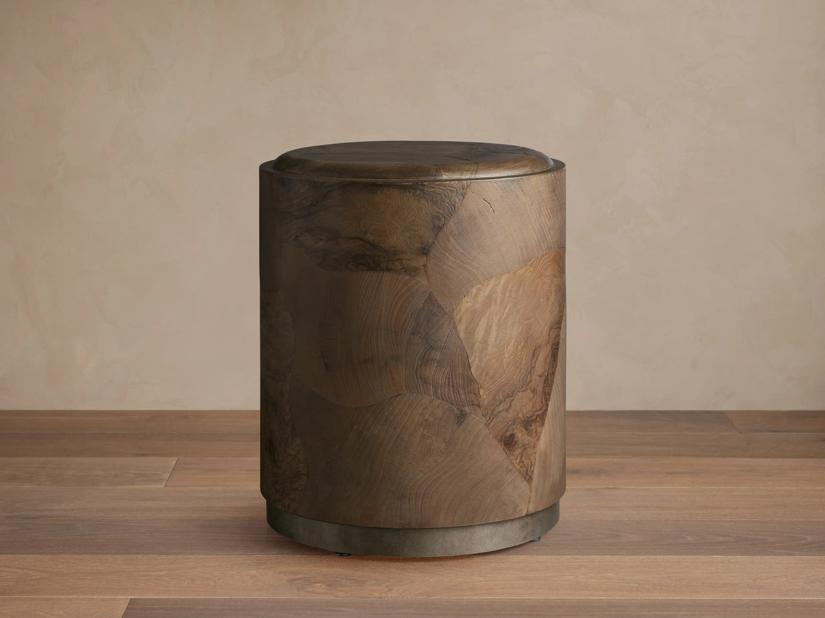 Polanco Round Plinth End Table, dark natural wood with oyster-cut fragments, cylindrical shape, on a weathered metal base.