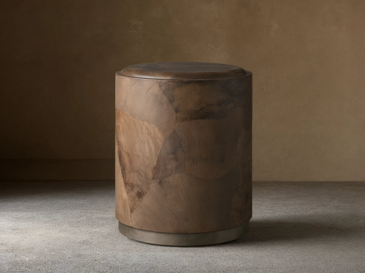 Polanco Round Plinth End Table, dark natural wood with oyster-cut fragments, cylindrical shape, on a weathered metal base.