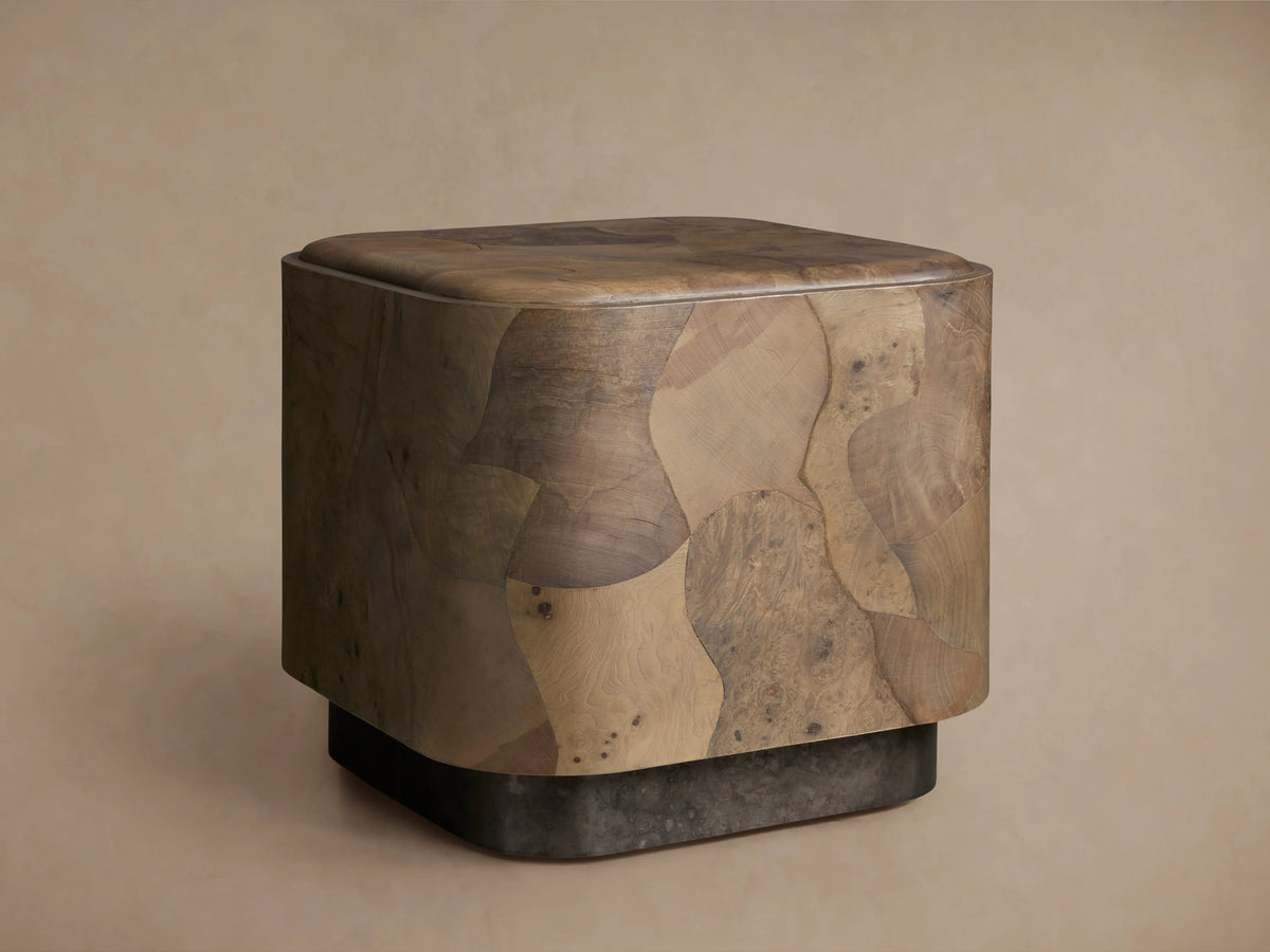 Polanco Plinth End Table, a block-shaped table with rounded edges, crafted from varied brown oyster-cut wood burl fragments. Dark plinth base.