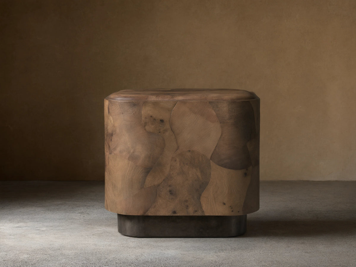 Polanco Plinth End Table, a block-shaped table with rounded edges, crafted from varied brown oyster-cut wood burl fragments. Dark plinth base.