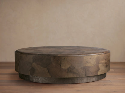 Round coffee table with smooth, curved edges and a textured surface. Made from ash wood fragments, showing tonal variations and natural patterns. Set on a weathered steel base with rich patina.