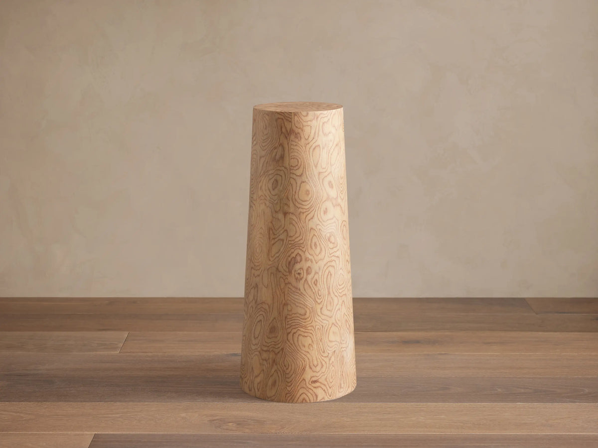 Redge Martini Table, a light-colored, tapered wood cylinder with swirling madrona burl grain, standing on a wooden floor.