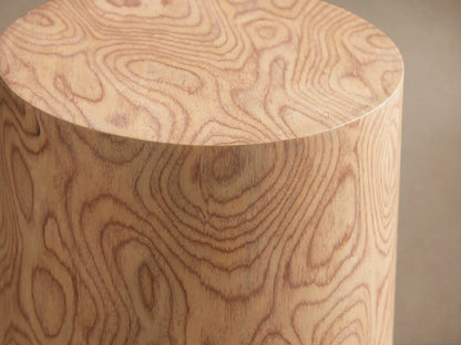 Redge Martini Table, a light-colored, tapered wood cylinder with swirling madrona burl grain, standing on a wooden floor.