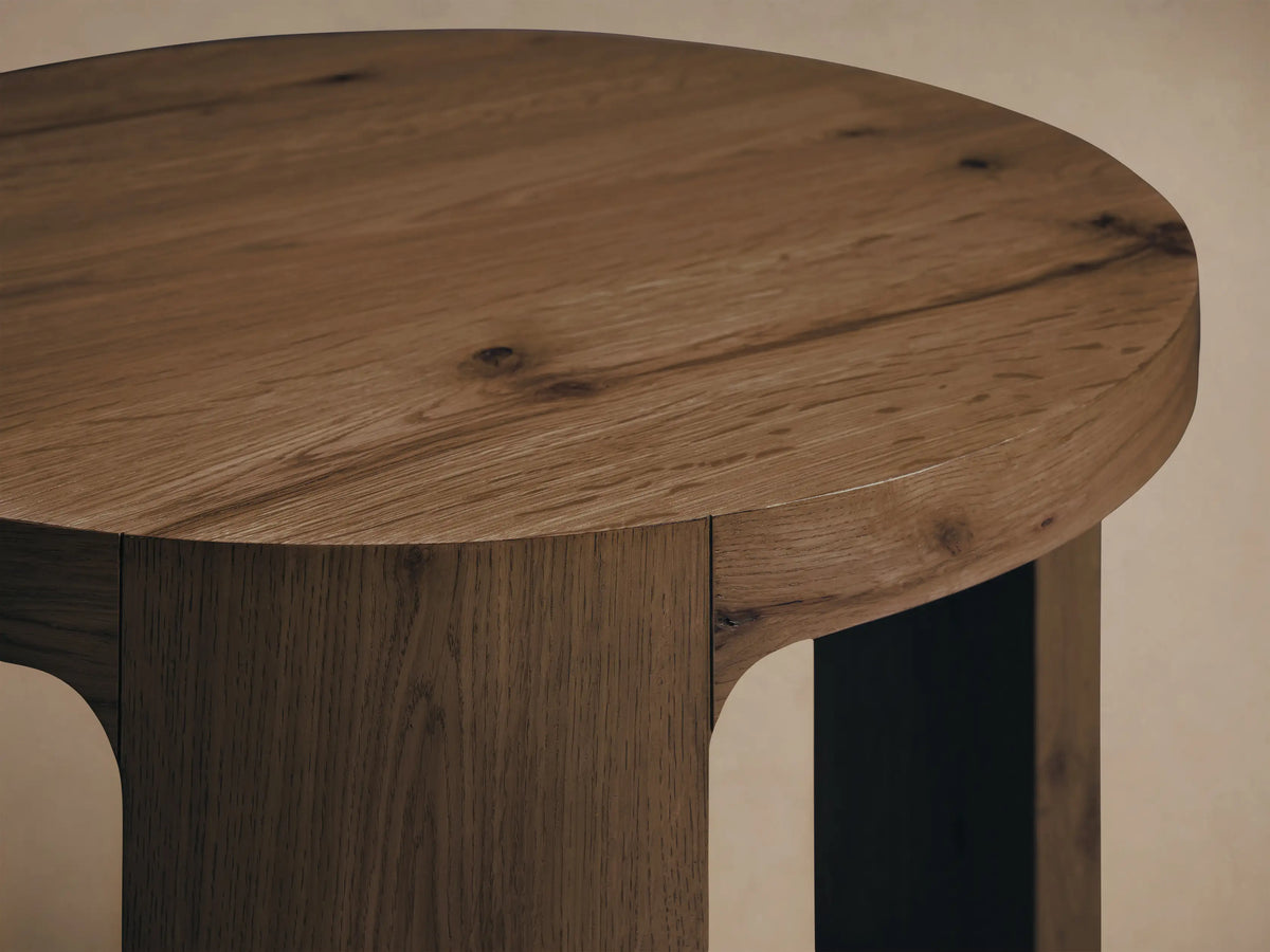 Front view of the round, light brown Redding End Table, featuring a built-in lower shelf and thick vertical supports.