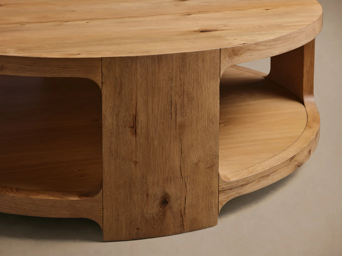 Close-up of the natural oak Redding Round Coffee Table, highlighting its distinct wood grain, curved side, and integrated lower shelf.