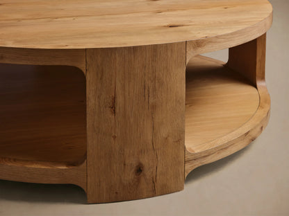 Close-up of the natural oak Redding Round Coffee Table, highlighting its distinct wood grain, curved side, and integrated lower shelf.