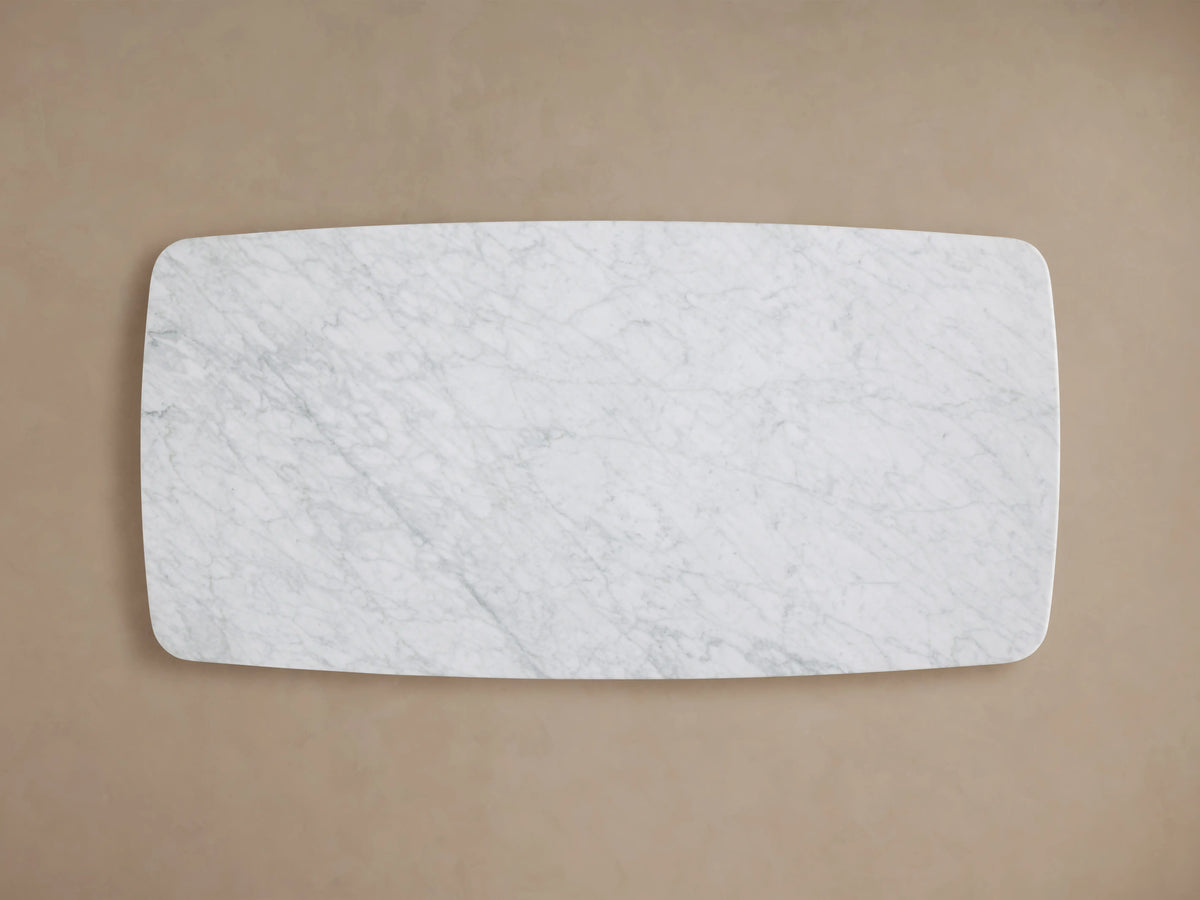 Rectangular coffee table with a Carrara marble top, showcasing light gray veining on a white surface. Rounded edges with a smooth finish.