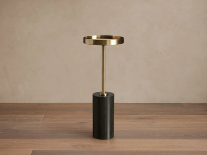 Rhodes Martini Table with a brass tray atop a slim stem and a black cylindrical marble base, set on a wooden floor.