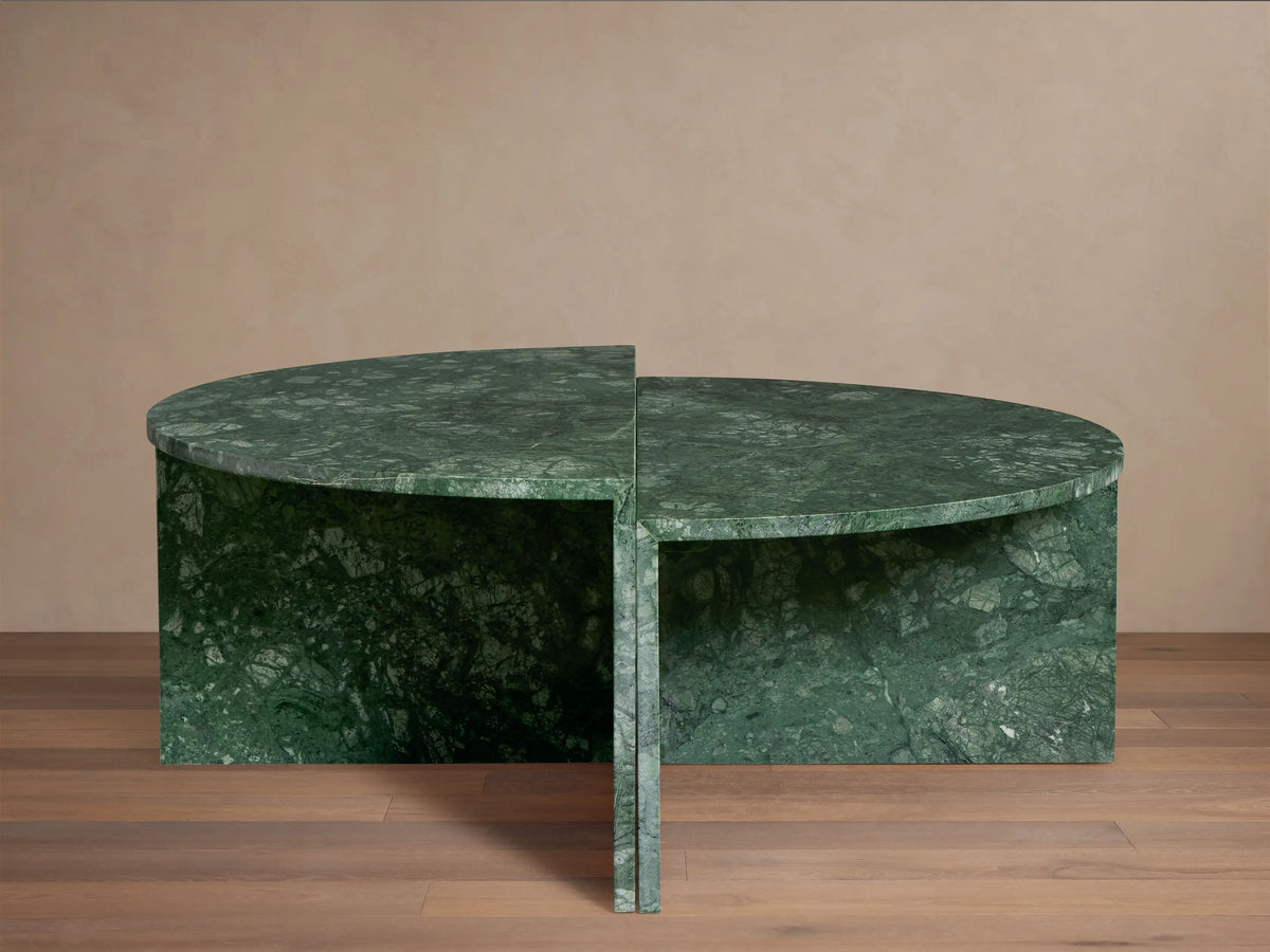 Green marble Riggs coffee table with a unique semi-circular design, standing on a wooden floor against a beige wall.