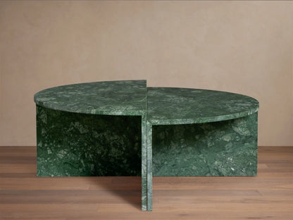 Green marble Riggs coffee table with a unique semi-circular design, standing on a wooden floor against a beige wall.
