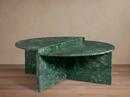 Green marble Riggs coffee table with a unique semi-circular design, standing on a wooden floor against a beige wall.