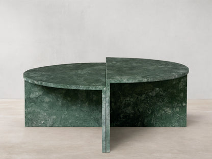 Green marble Riggs coffee table with a unique semi-circular design, standing on a wooden floor against a beige wall.