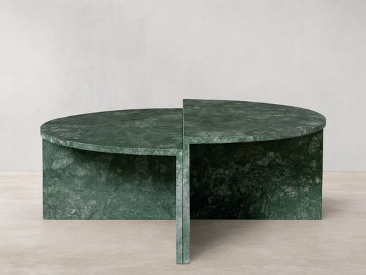 Green marble Riggs coffee table with a unique semi-circular design, standing on a wooden floor against a beige wall.