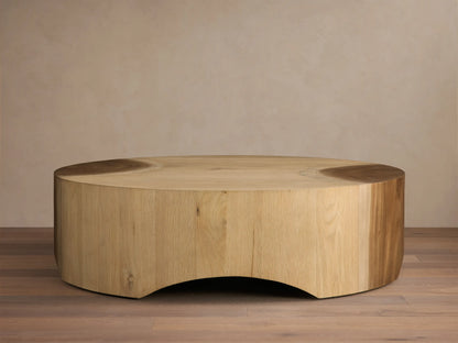 Front view of a light wood coffee table, round with a solid, inwardly curved base, showcasing subtle top surface details.