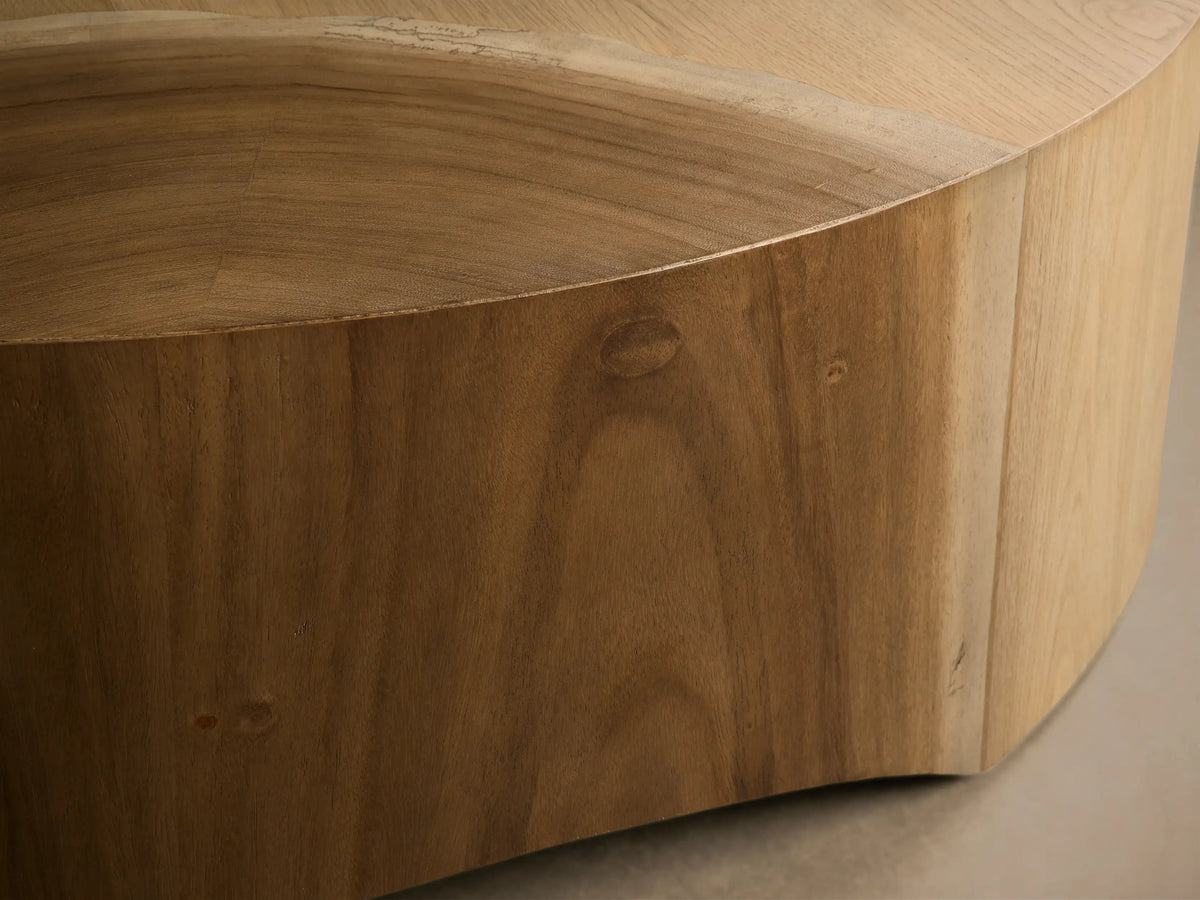 Front view of a light brown wood coffee table with a round drum base and curved cut-out bottom.